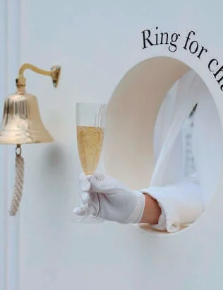 Campainha dourada e taça de champagne servida pela abertura da parede